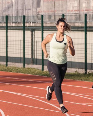 Genç, güçlü, kararlı Kafkas bayan atlet koşu pistinde dördüncü kulvarda koşu pozisyonunda başlıyor.