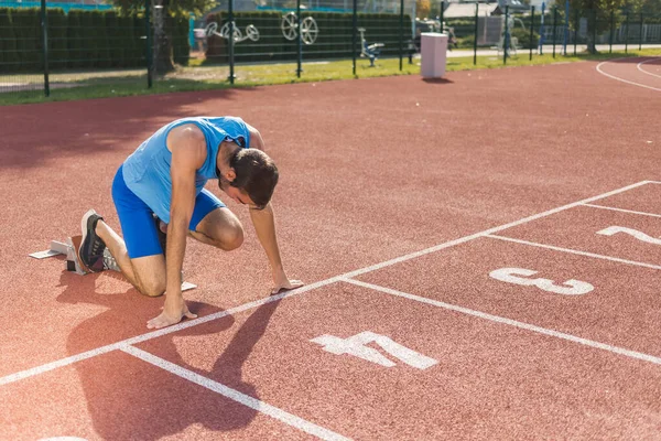 stock image Young professional male athlete in blue sportswear taking a start position for a sprint run during outdoor training