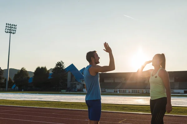 Young sport couple training on athletic stadium giving high five at sunset