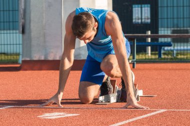 Koşu için antrenman yapan genç adam dışarıda bir stadyum pistinde başlıyor.