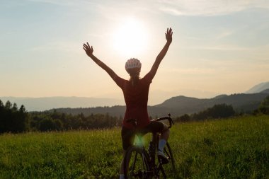 Başarılı bir şekilde hedefe ulaştıktan sonra kollarını başının üstüne kaldıran mutlu bir kadın yol yarışı bisikletçisi.