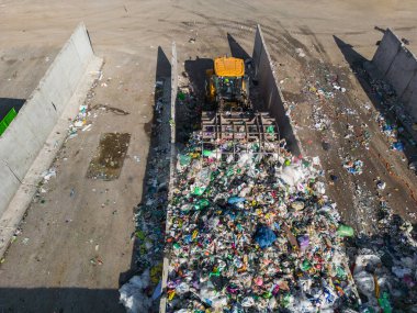 Skid steer loader moving plastic garbage with scrap grapple on the landfill site, drone shot. Waste disposal concept.