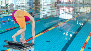 Profesyonel sporcu kadın başlangıç bloğunda sağlam bir duruş sergiliyor, dalıyor ve havuz suyuna çarpıyor..