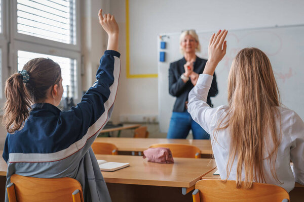 Female student raising her hand and answering a cheerful smiling teachers question. Motivation, education, and class activity concepts.