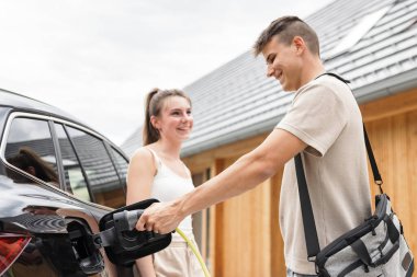 Kadın ve erkek elektrikli arabayı şarj ediyor. Yenilenebilir enerji kavramı.