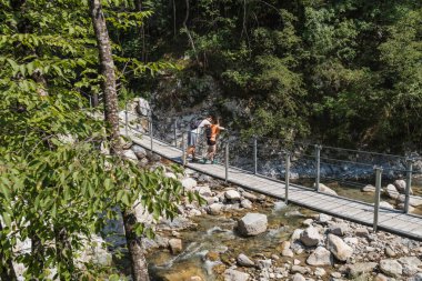 Aktif genç yürüyüşçüler, kadın ve erkek büyük kayaların arasında akan bir dağ deresinin üzerinde yürüyorlar. Doğa keşfi kavramı.