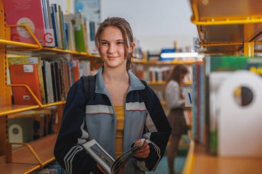 Okul kütüphanesinde kitap okuyup heyecan verici edebiyat arayışında olan güzel bir genç kızın portresi.