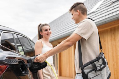 Kadın ve erkek elektrikli arabayı şarj ediyor. Yenilenebilir enerji kavramı.