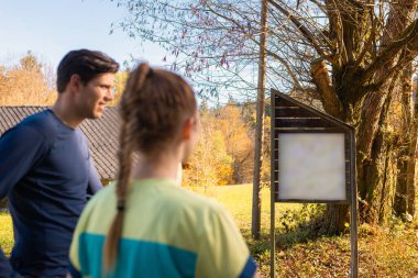 Yürüyüşçü kadın ve erkek doğadaki bilgi panosuna bakıyorlar.