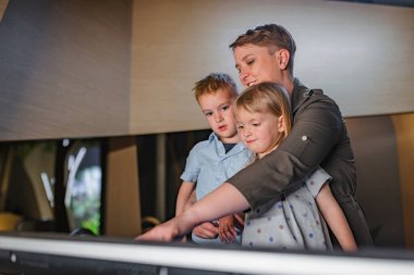 Aile doğal tarih müzesini ziyaret ediyor, iki çocuklu bir anne dijital etkileşimli ekranın önünde duruyor..