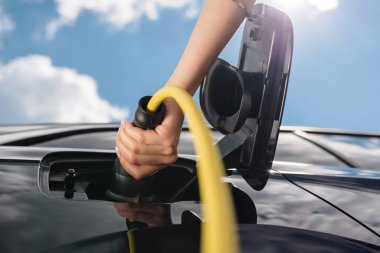 Şehirde park halindeki elektrikli arabayı şarj eden genç bir kadın yenilenebilir enerji kullanıyor..