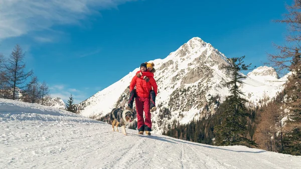 Man carries his girlfriend on his back in snowy mountain area with dog