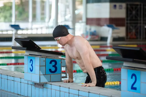 Fit strong swimmer with a black swimming cap looking at the pool with swimming goggles.