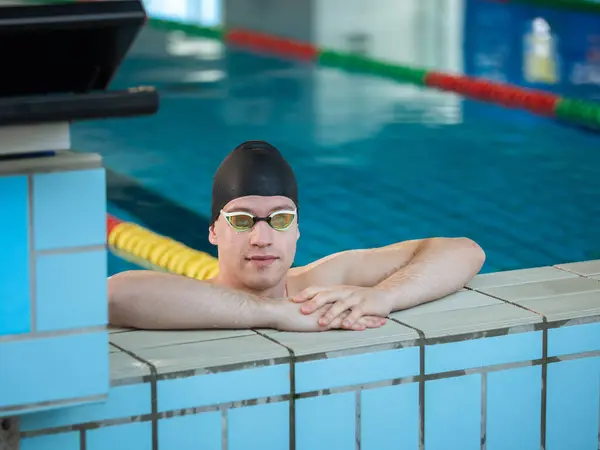 Fit strong swimmer with a black swimming cap looking at the pool with swimming goggles.