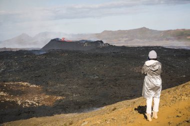 Karanlık volkanik manzaraya bakan kadın turist kraterde parlayan erimiş lav, İzlanda 'daki patlamalar sırasında aktif volkan.