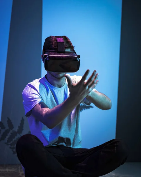 Young man wearing VR glasses sitting in a yoga pose on the virtual reality escape room floor. Fun, entertainment, and innovation concepts.