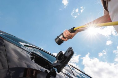 Kadın elektrikli araba açıyor, prizi şarj ediyor ve şarj aletini takıyor.