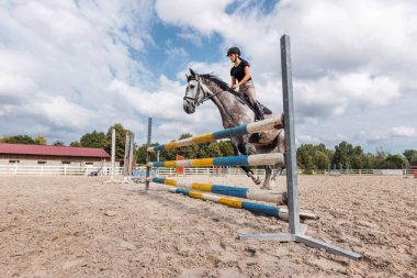 Binicilik merkezinin sondaj salonunda çitlerden atlama alıştırması yapan gri atlı bir kız. Gösteri atlayışı ve olay kavramları.