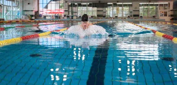 Front view of a male athlete swimming breaststroke style in the pool between two swimming lane markers. Competitive swim discipline concept.
