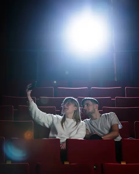 Young teenager couple in love at cinema having fun watching a film in the empty movie place. Entertainment and people concept.