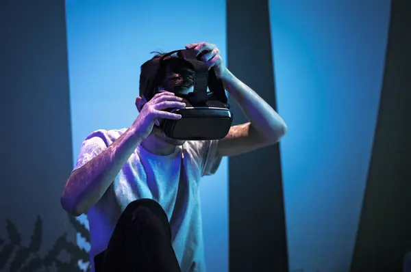 Young man wearing VR glasses sitting in a yoga pose on the virtual reality escape room floor. Fun, entertainment, and innovation concepts.