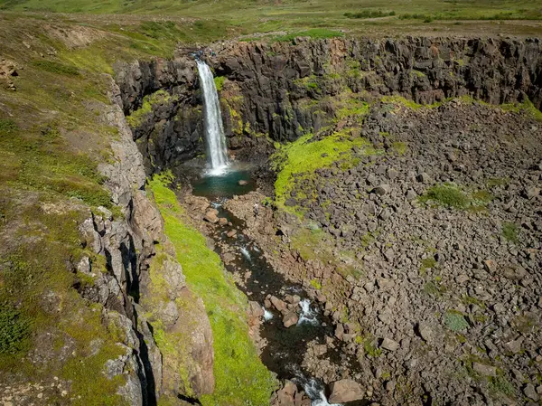 Stunning Iceland waterfall with icy cold water and the pool at the base filled with rocks on a sunny day, aerial view. Travel destination and nature wonder concepts.
