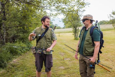 Nehir kıyısında kıdemli ve genç balıkçılar balık tutarken ve konuşurken eğleniyorlar. Doğada keyif ve eğlence kavramları.
