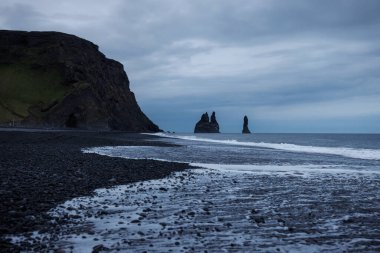 Reynisfjara sahilinin ikonik manzarası İzlanda 'da, siyah volkanik kum, bazalt kayalar ve Atlantik Okyanusu' ndaki kayalar ile güzel bir kıyı şeridi..