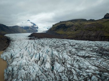 Eriyen buzulun yüzeyi, volkanik kül tabakalı siyah beyaz buz ve çatlaklarda turkuaz su, havadan aşağıya doğru çekim. Doğa arkaplan kavramı.