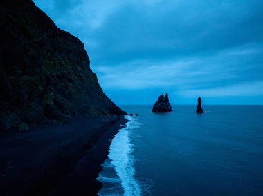 Reynisfjara sahilinin ikonik manzarası İzlanda 'da, siyah volkanik kum, bazalt kayalar ve Atlantik Okyanusu' ndaki kayalar ile güzel bir kıyı şeridi..