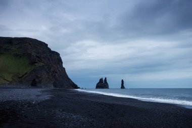 Reynisfjara sahilinin ikonik manzarası İzlanda 'da, siyah volkanik kum, bazalt kayalar ve Atlantik Okyanusu' ndaki kayalar ile güzel bir kıyı şeridi..
