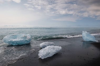Buzdağının buzdağının parçaları İzlanda 'da muhteşem bir kara kumsalda okyanusa dökülüyor. Seyahat, eşsiz deneyim ve kış mevsimi konsepti.