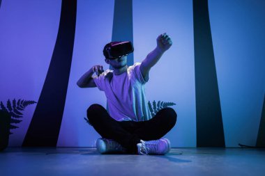 Sanal gerçeklik kaçış odasının zemininde yoga pozunda oturan VR gözlüklü genç adam. Eğlence, eğlence ve yenilik kavramları.