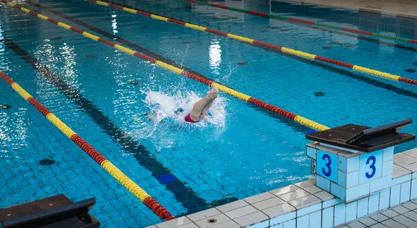 Sportswoman, a professional swimmer at the start of the swimming race, beginning drive from the block, flighting and entering into the pool water