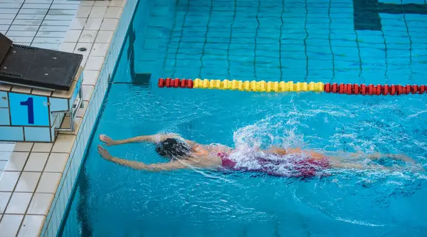 Professional sportswoman, a swimmer during freestyle swimming training, ultimate sports drills in the pool, side shot. Disciplane and practice concept.