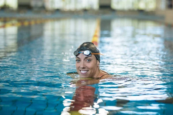 Portrait of a woman, a professional swimmer in black one-piece swimwear and a black cap with goggles