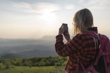 Ergenlik çağındaki kız, akıllı telefonuyla gün batımında fantastik dağ manzarasının fotoğraflarını çekiyor.