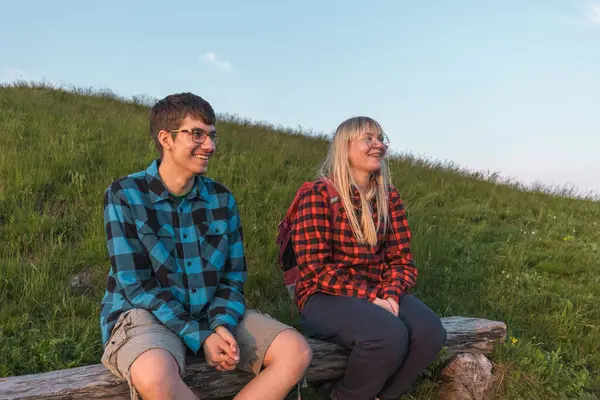 Young couple enjoying the fantastic mountain panorama at sunset while sitting on the bench at a viewpoint. Picturesque moments and natural beauty concepts.