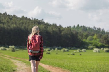 Yürüyüş yapan genç bir kadın doğa manzarasına bakıyor.