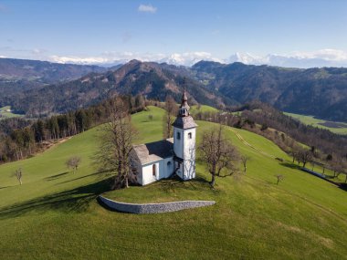 Slovenya 'daki ünlü yerin havadan görünüşü, Saint Thomas' ın tepedeki beyaz kilisesi, Alp dağlarının muhteşem insansız hava aracı manzarasıyla çevrili..