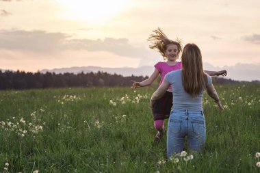 Anne ve küçük kızı gün batımında yeşil bir tarlada nazikçe kucaklaşıyorlar. Ebeveynler ve çocuklar arasındaki ilişki kavramı.
