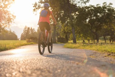 Güzel bir günbatımında kırsal yolda elektrikli dağ bisikleti süren bir kadın silueti.