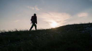 Sırt çantalı bir kadın yürüyüşçü silueti yukarı doğru yürüyor ve gün batımında gökyüzünün tadını çıkarıyor. İlham ve sağlıklı yaşam tarzı kavramları.