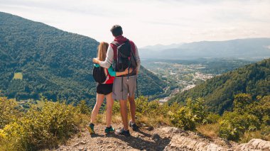 Genç, kucaklaşan çift, güneşli bir yaz günü yürüyüş sonrası bir bakış açısına ara vererek, fantastik dağ ve vadi manzarasının tadını çıkarıyorlar.