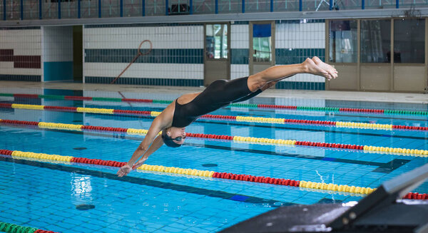 Professional female swimmer preparing and jumping off the starting block into the pool. Competitive swimmers workout concept.