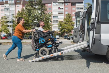 Engelli bir adam, tekerlekli sandalye kullanıcısı kız arkadaşının yardımı ve ulaşım rampasıyla ulaşılabilir bir araca biniyor..
