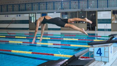 Profesyonel bayan yüzücü başlangıç bloğundan havuza atlamaya hazırlanıyor. Rekabetçi yüzücüler egzersiz konsepti.