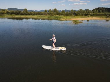 Paddleboarder paddling a sup board on a beautiful calm mountain lake at summer sunset, aerial view. Nature and healthy lifestyles concepts. clipart