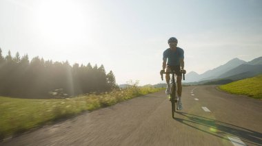 Mavi formalı ve teçhizatlı bir sporcu kaldırımlı yolda profesyonel bir yarış bisikletine biniyor.