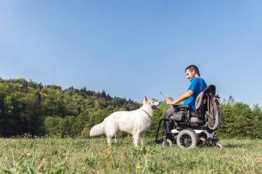 Özürlü bir adam güzel bir doğa ortamında evcil köpeğiyle oynuyor. Hayvanlar ve insanlar arkadaşlık kavramı.